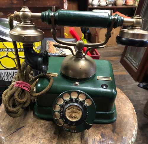 A vintage green rotary phone with a brass receiver and dial, resting on a wooden surface.