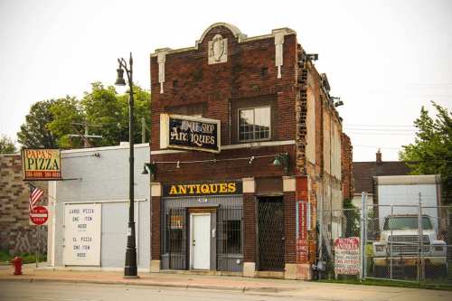 A vintage brick building with an "Antiques" sign, next to a pizza shop, showing signs of wear and age.