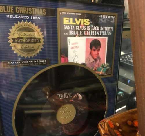 Gold record plaque for Elvis's "Blue Christmas," featuring the 45 RPM single cover and decorative items in the background.