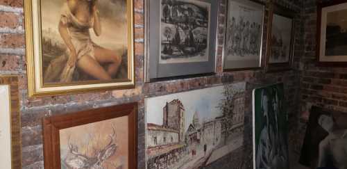 A collection of framed artworks displayed on a brick wall, featuring various styles and subjects.