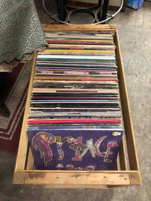 A wooden crate filled with colorful vinyl records, featuring a prominent album cover by Prince on top.