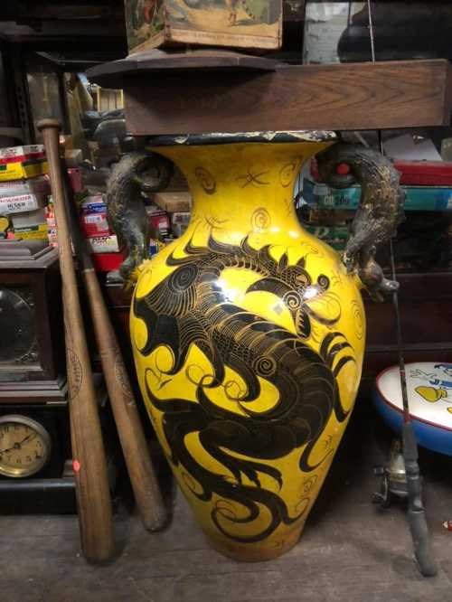 A large yellow vase with black dragon designs, surrounded by various antiques and collectibles in a cluttered space.