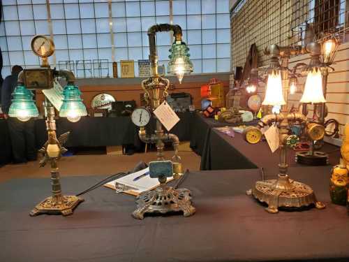 Three unique vintage lamps made from pipes and gauges, displayed on a table with various other items in the background.