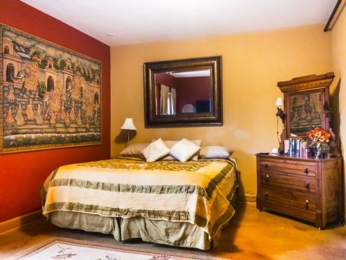 Cozy bedroom with a large bed, decorative wall art, a mirror, and wooden furniture in warm tones.