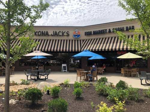 Exterior of Kona Jack's Fish Market & Sushi Bar, featuring outdoor seating and colorful umbrellas under a cloudy sky.