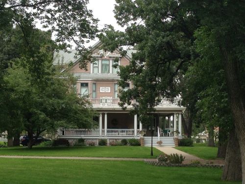 A large, historic house with a wraparound porch, surrounded by trees and a green lawn.