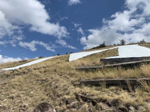 A grassy hillside with large white letters painted on it, under a blue sky with scattered clouds.