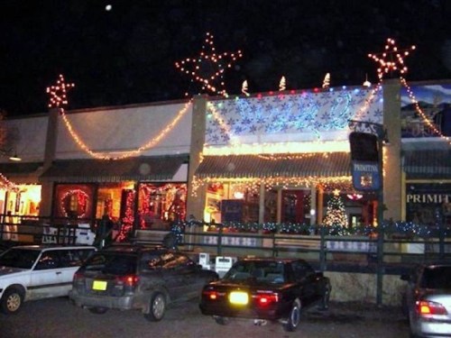 A festive storefront decorated with colorful lights and stars, surrounded by parked cars at night.