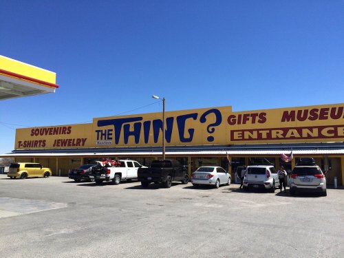 A colorful storefront labeled "THE THING?" with signs for souvenirs, gifts, and a museum, surrounded by parked cars.