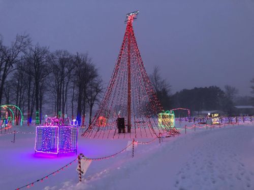 A snowy landscape featuring colorful holiday lights and a tall, illuminated Christmas tree.