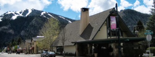 A quaint building on a street with mountains in the background, featuring snow-capped peaks and a clear blue sky.