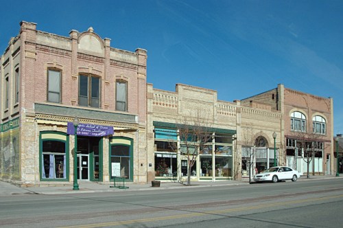 Historic brick buildings line a street, featuring storefronts and a clear blue sky above.