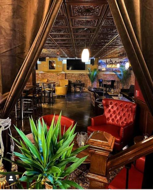 Cozy restaurant interior with rich decor, plush seating, and a warm ambiance, framed by curtains and greenery.