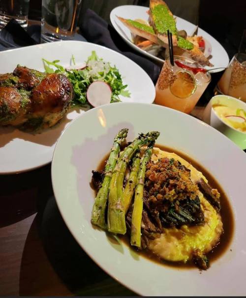 A beautifully plated meal featuring roasted chicken, salad, asparagus, and a savory dish with mashed potatoes and sauce.