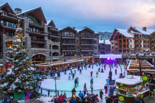 A festive outdoor ice skating rink surrounded by snow-covered buildings and holiday decorations.