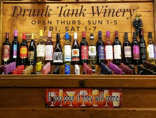 A wooden display at Drunk Tank Winery featuring various wine bottles and a sign that reads, "If you pour it, they will come."