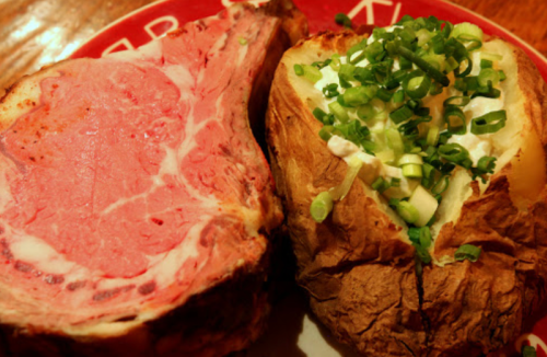 A plate featuring a juicy prime rib steak alongside a baked potato topped with sour cream and green onions.