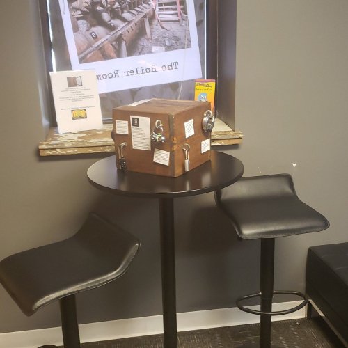 A small table with two chairs, featuring a locked box and a window displaying a wooden interior.