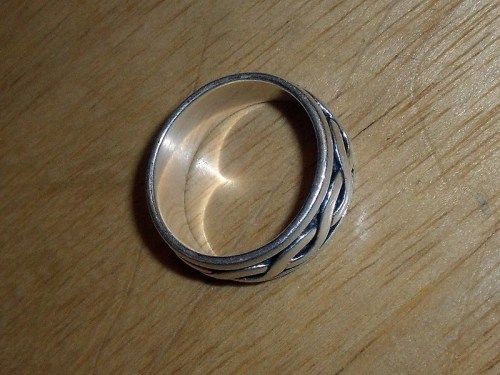 A silver ring with a twisted design resting on a wooden surface.