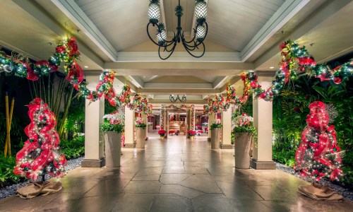A festive hallway adorned with red and green decorations, lights, and floral arrangements, creating a holiday atmosphere.