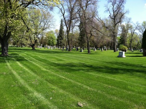 A peaceful cemetery with neatly mowed green grass, trees, and gravestones scattered throughout the landscape.