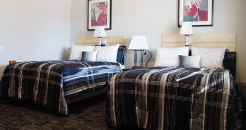 A hotel room featuring two beds with plaid bedding, bedside lamps, and framed artwork on the walls.
