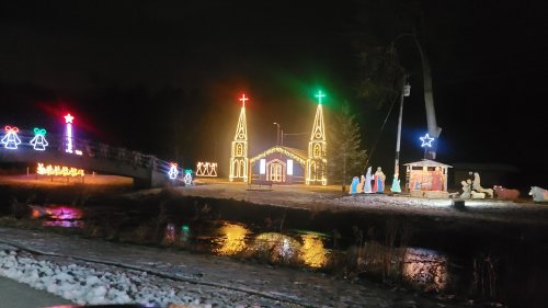 A festive scene at night featuring illuminated churches, holiday decorations, and a nativity display by a river.
