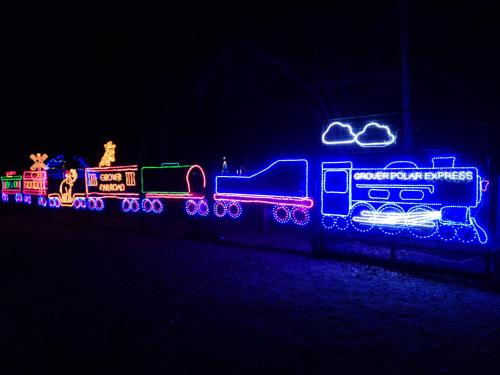A colorful display of Christmas lights shaped like a train, featuring festive designs against a dark night sky.