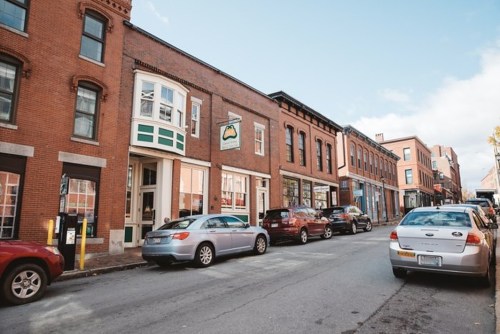 A charming street lined with brick buildings and parked cars under a clear blue sky.