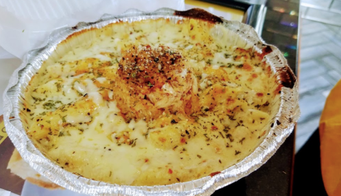 A baked dish in a silver foil container, topped with herbs and a crispy topping, featuring creamy cheese and pasta.