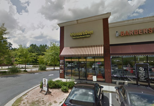 Exterior of Moreau's Oven restaurant with a sign, surrounded by trees and parked cars under a cloudy sky.