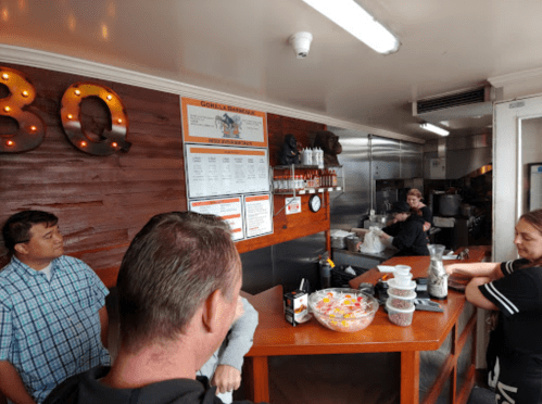 A busy BBQ restaurant interior with customers at the counter and staff preparing food in the background.