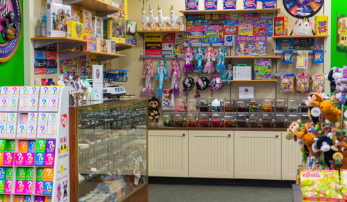 A colorful candy store interior featuring shelves of sweets, toys, and a glass display case with treats.