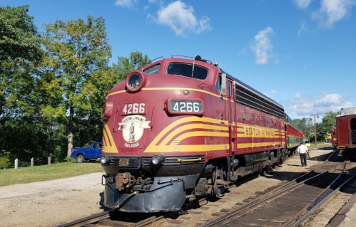 A vintage red and yellow train engine numbered 4266 parked on tracks, surrounded by trees and a clear blue sky.