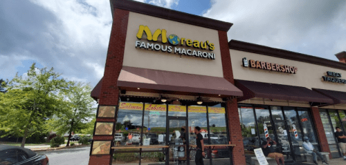 Exterior of a restaurant named "Moread's Famous Macaroni," featuring a barbershop next door and a cloudy sky.