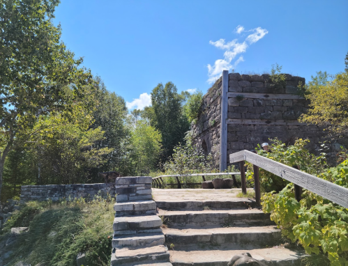 Stone steps lead up to ancient ruins surrounded by lush greenery and a clear blue sky.
