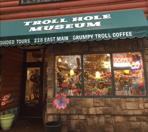 Exterior of the Troll Hole Museum with a green awning, colorful decorations, and a sign for Grumpy Troll Coffee.