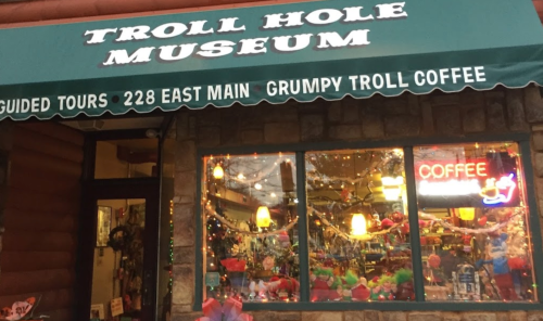 Exterior of the Troll Hole Museum with a green awning, colorful decorations, and a neon coffee sign in the window.