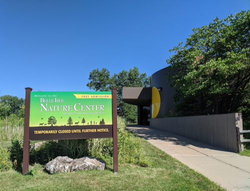 Sign for Belle Isle Nature Center, stating it's temporarily closed, with a clear blue sky and greenery in the background.