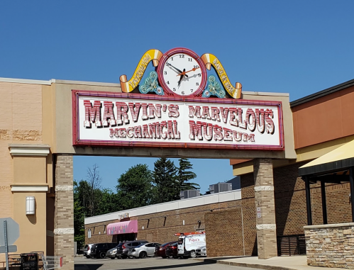 Sign for Marvin's Marvelous Mechanical Museum, featuring a clock and colorful lettering, against a clear blue sky.