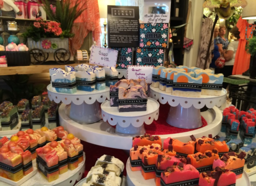 A colorful display of artisanal soaps arranged on white pedestals, surrounded by floral decorations.