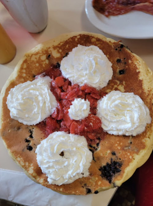 A large pancake topped with whipped cream and strawberry topping arranged in a flower pattern.