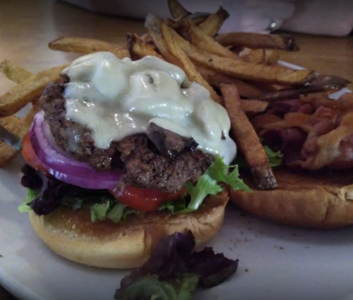 A close-up of a burger with lettuce, tomato, onion, and creamy sauce, served with a side of crispy fries.