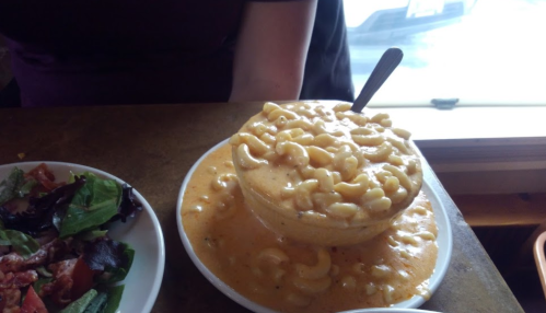 A large bowl overflowing with macaroni and cheese, next to a plate of salad with mixed greens and tomatoes.