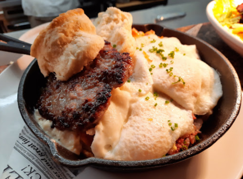 A cast iron skillet filled with creamy dish topped with a biscuit and garnished with chives.