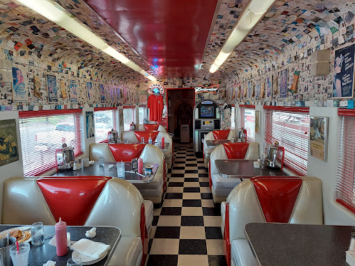 A retro diner interior with red and white booths, checkered floor, and walls covered in photos and memorabilia.
