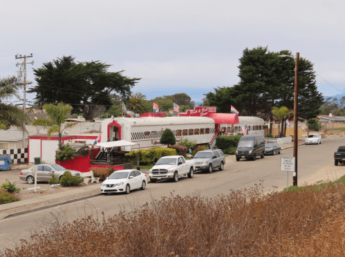 A vintage diner shaped like a train, surrounded by palm trees and parked cars along a quiet street.