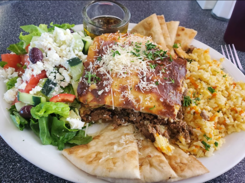 A plate of food featuring a baked dish, rice, pita bread, and a fresh salad with feta cheese and dressing.