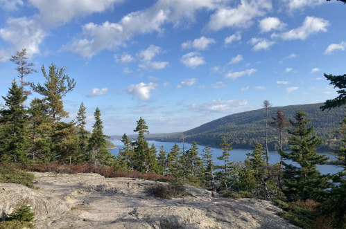 A scenic view of a lake surrounded by trees and hills under a partly cloudy sky.