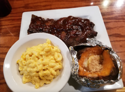 A plate featuring barbecue ribs, creamy macaroni and cheese, and a baked sweet potato topped with brown sugar.